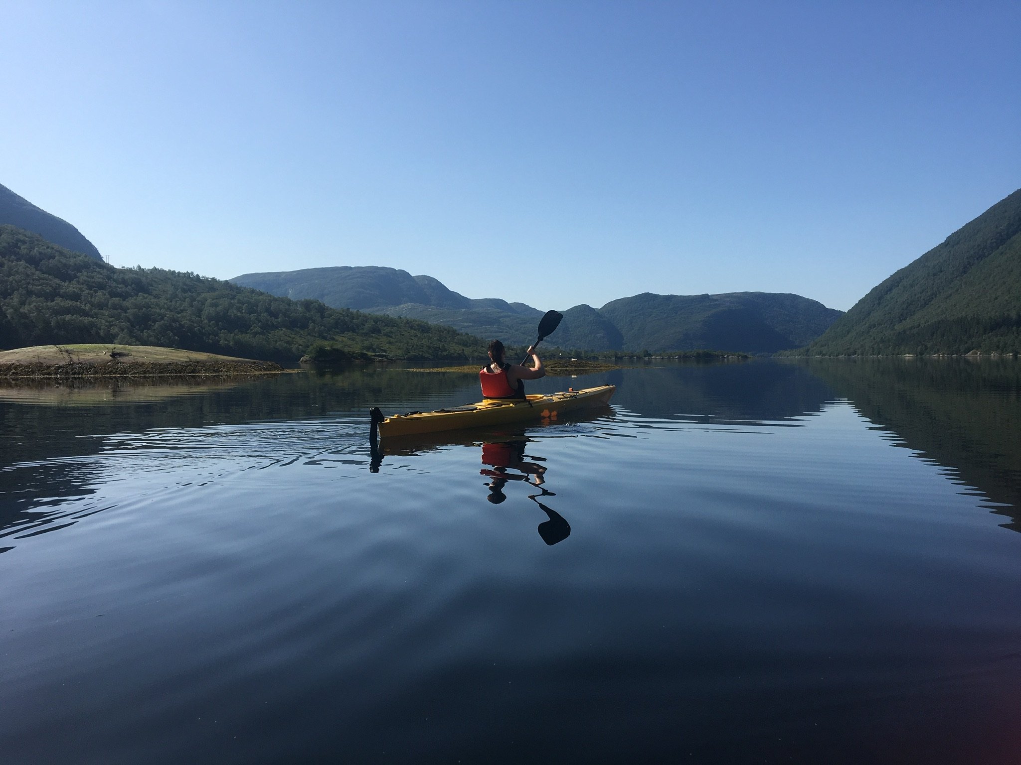 A kayaker on mirror-still fjord water between high mountains