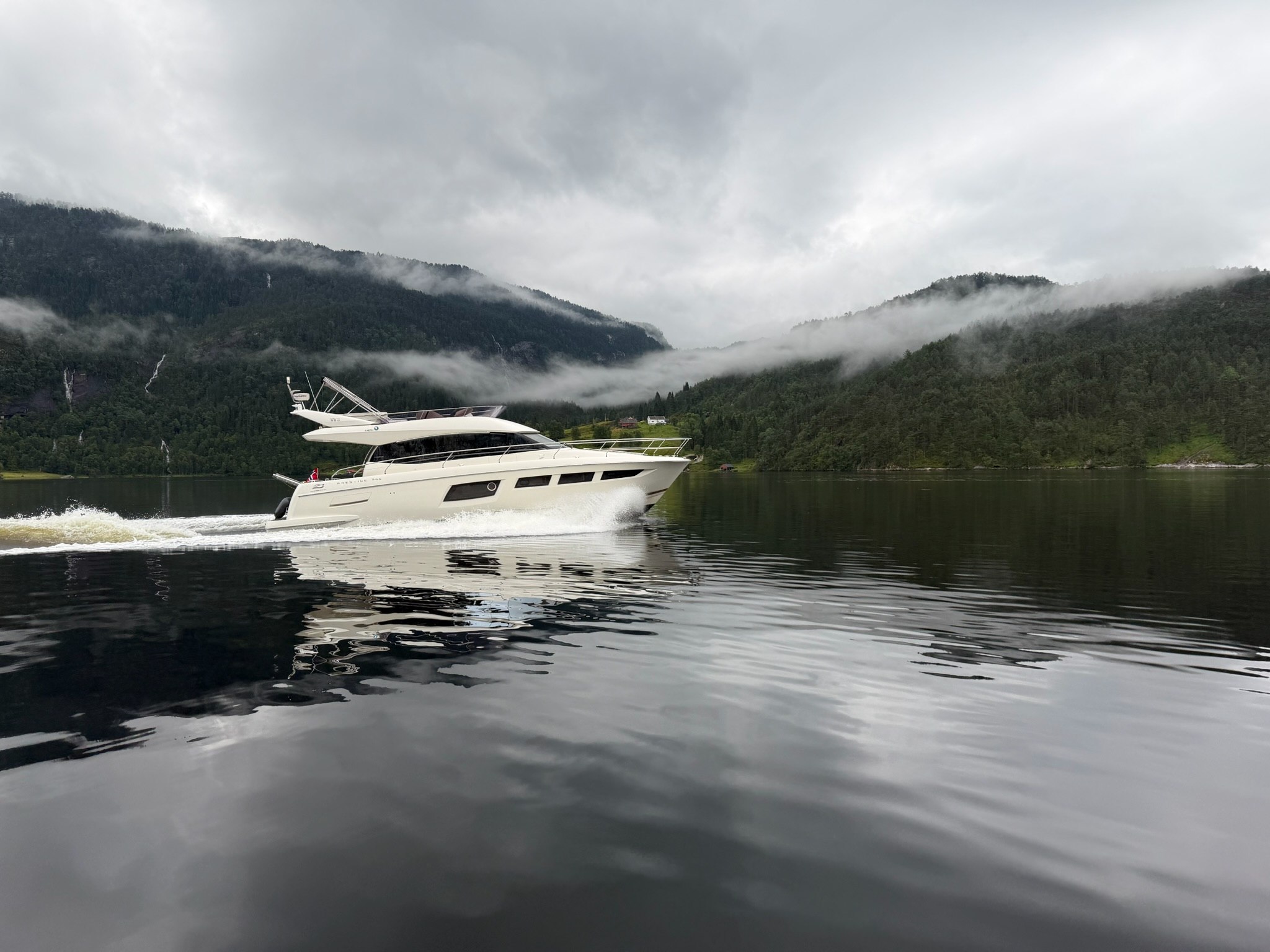 Fjord Queen under way on still water, mist on the hillsides behind